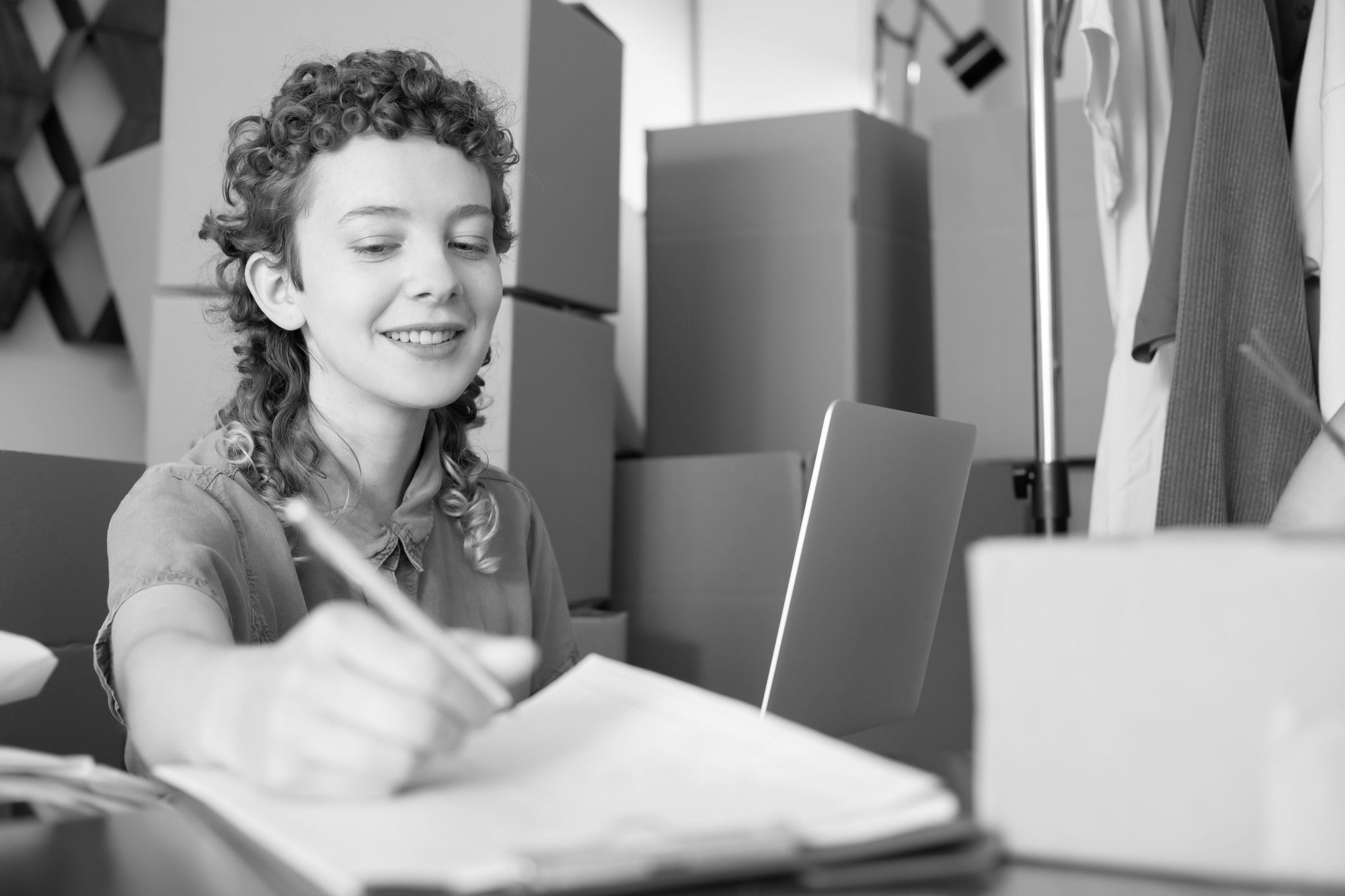A woman writing at a desk with a laptop and parcels